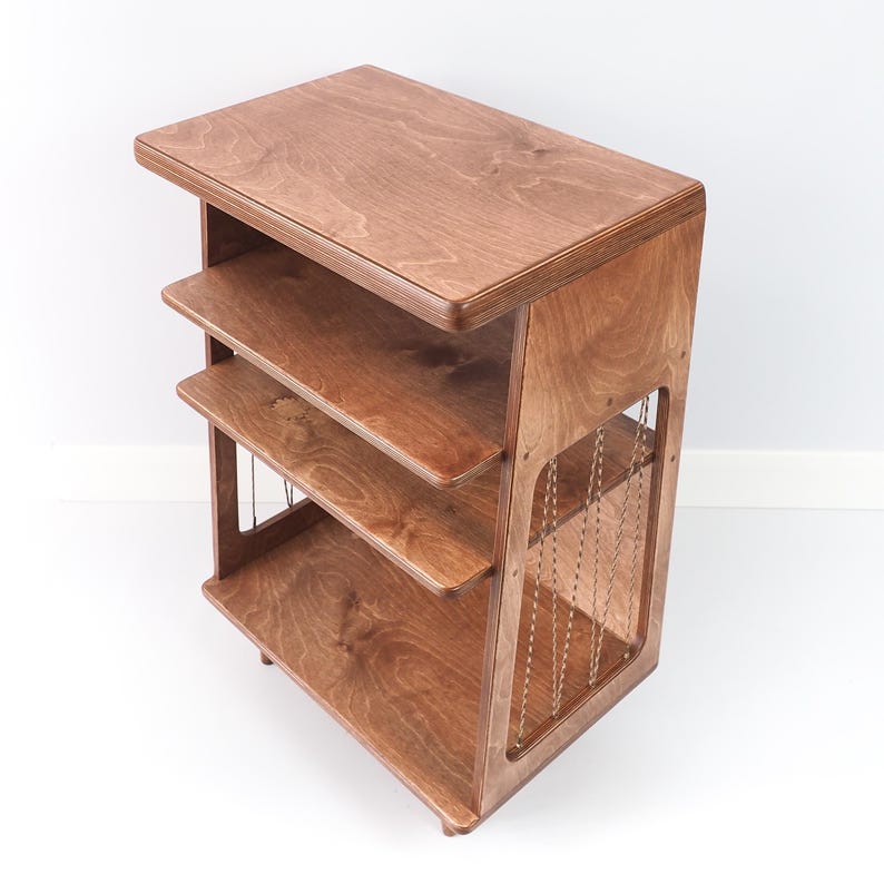 May include: A brown wooden shelving unit featuring a flat top surface and two lower shelves. The side panels are constructed with a cutout design, accented by thin, vertical, light-coloured cord detailing that connects the top to the base.