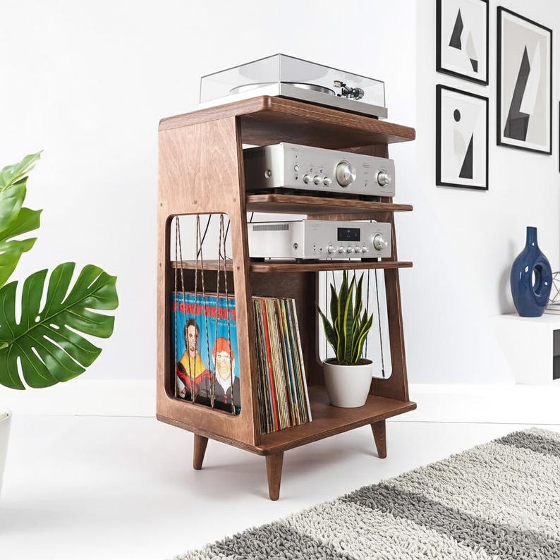 May include: A wooden media console with four tiers, featuring a top turntable, two silver audio components, and a bottom shelf for vinyl records. The side panels have vertical string detailing, and the unit stands on four tapered wooden legs.