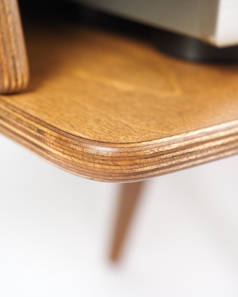 Peut inclure: Gros plan sur un coin de table en bois. La table a une finition brun clair avec un grain de bois visible et un bord arrondi. La construction en couches de la table est &eacute;vidente, et un pied est visible.