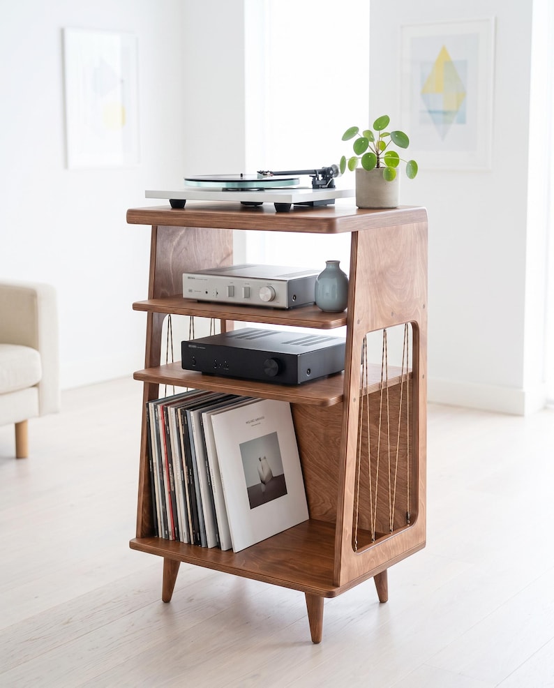May include: A wooden media console with four tiers, featuring a white turntable on the top shelf, silver and black audio components on the middle shelves, and a collection of vinyl records stored vertically on the bottom shelf with side cord detailing.
