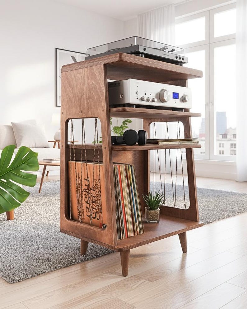 May include: A brown wooden media console with four tiers, featuring a top surface for a turntable, a middle shelf for an amplifier, and lower sections with vertical cord dividers for vinyl record storage, supported by four tapered wooden legs.