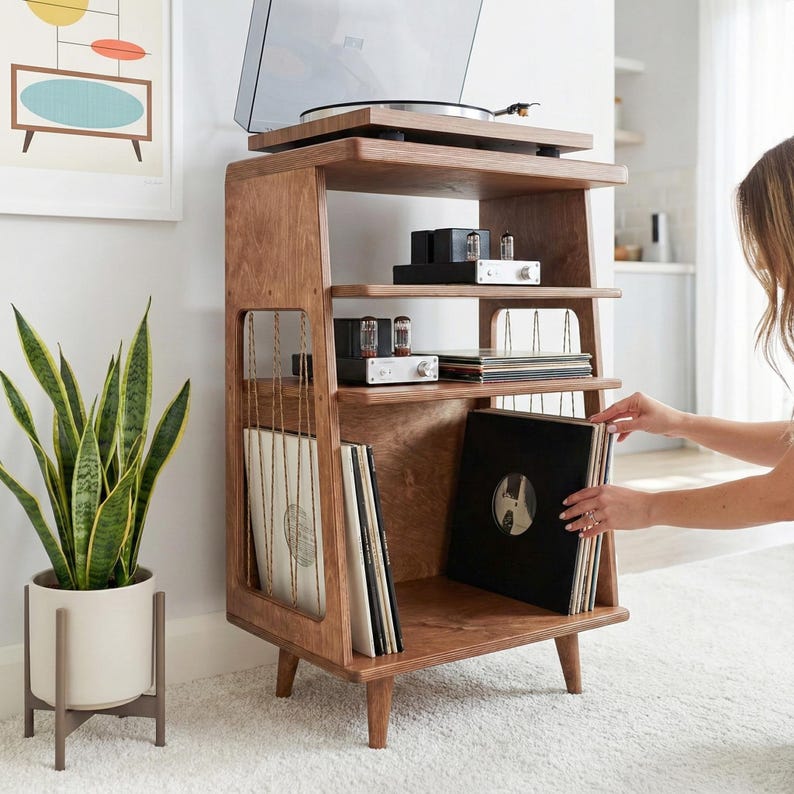 May include: A wooden record player stand with four tapered legs, featuring a top surface for a turntable, two middle shelves for audio equipment, and a bottom section with vertical string dividers for organising vinyl record albums.