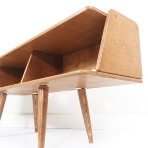 Peut inclure: Biblioth&egrave;que en bois de style moderne du milieu du si&egrave;cle, de couleur marron clair. Elle comporte trois compartiments et repose sur quatre pieds effil&eacute;s et inclin&eacute;s. Le design pr&eacute;sente des bords arrondis et une esth&eacute;tique minimaliste. Mesure environ 120 cm de long.