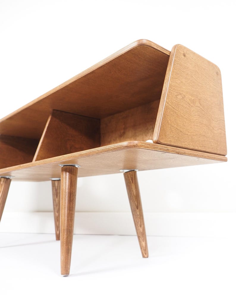 Peut inclure: Biblioth&egrave;que en bois de style moderne du milieu du si&egrave;cle, de couleur marron clair. Elle comporte trois compartiments et repose sur quatre pieds effil&eacute;s et inclin&eacute;s. Le design pr&eacute;sente des bords arrondis et une esth&eacute;tique minimaliste. Mesure environ 120 cm de long.