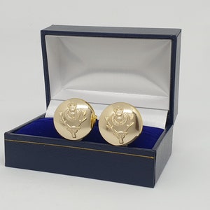 May include: Gold cufflinks in a blue box. The cufflinks feature a raised design of a crowned thistle with a stag's head.