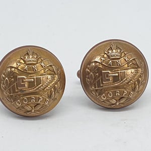 Puede incluir: Dos botones antiguos de latón con la inscripción "TANK CORPS" y un diseño de tanque. Los botones son redondos y tienen un diseño en relieve detallado. Probablemente botones de uniforme militar vintage.