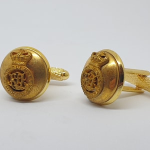 May include: A pair of gold cufflinks featuring a royal crest design. The crest includes a crown and the letters "ER" within a circle.