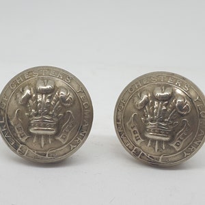 Puede incluir: Dos botones de metal plateado con la inscripción "Earl of Chester's Yeomanry" y un diseño de corona.