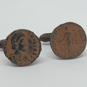 Op de afbeelding: Paar manchetknopen in antieke stijl met ronde, bronskleurige muntontwerpen. Eén manchetknop toont een profielportret, de andere een staande figuur. De manchetknopen hebben een getextureerde, donkerbruine steel.