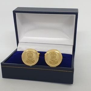Può includere: Un paio di gemelli d'oro in una scatola di velluto blu. I gemelli presentano un design a corona e ancora d'oro.