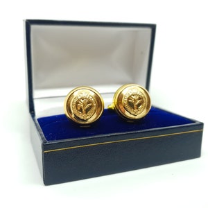 May include: A pair of gold cufflinks in a blue velvet box. The cufflinks feature a gold design of a thistle.
