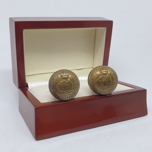 Puede incluir: Un par de gemelos dorados en una caja de madera roja. Los gemelos presentan un diseño de una corona y las palabras "Australian Military Forces".