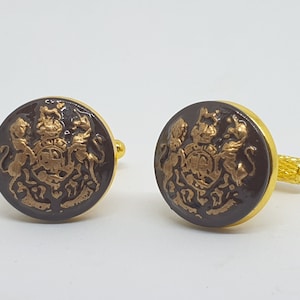 Puede incluir: Un par de gemelos de oro con un diseño de esmalte marrón que presenta un escudo con dos leones y una corona.