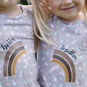 May include: Two grey sleeveless shirts with a rainbow design and the words "better" and "together" printed on them. The shirts have a floral pattern with butterflies.