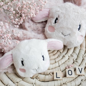 Könnte beinhalten: Zwei Plüsch-Lammspielzeuge mit rosa Ohren und gestickten Gesichtern, die auf einem geflochtenen Korb mit dem Wort "LOVE" in Holzblöcken liegen.