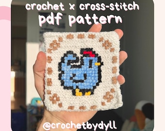 May include: A crochet and cross-stitch pattern for a blue chicken with a red comb. The pattern is framed with a brown border and is held in a hand. The text "crochet x cross-stitch pdf pattern" and "@crochetbydyll" are visible.