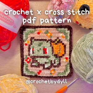 Puede incluir: Un patrón de ganchillo cuadrado, afelpado, verde y naranja con un personaje de dibujos animados. El texto "crochet x cross stitch pdf pattern" está en la parte superior. El identificador de Instagram "@crochetbydyll" está en la parte inferior. También se ven hilo y un ganchillo.