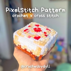 May include: A crocheted square cake with white, tan, red, and brown colors. The cake has a pixelated design, with the text "PixelStitch Pattern crochet x cross stitch" at the top. The Instagram handle "@crochetbydyll" is at the bottom.
