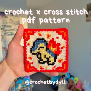 May include: A square, crocheted item with a pixelated design of a cartoon character, framed by a red border. The character is yellow, blue, and black, with a flame detail. The text "crochet x cross stitch pdf pattern" is above the item.