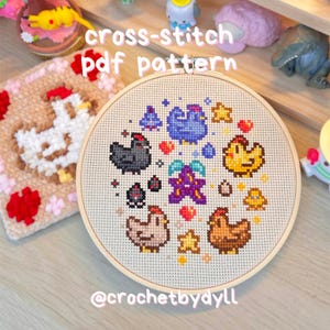 Puede incluir: Un patrón PDF de punto de cruz con un diseño circular de pollos y estrellas en un bastidor de bordado de madera. El texto "cross-stitch pdf pattern" es visible. El diseño incluye pollos negros, marrones, amarillos y azules. El texto "@crochetbydll" es visible.