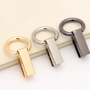May include: Three metal bag handles with a ring and a rectangular bar. The handles are gold, silver, and black.