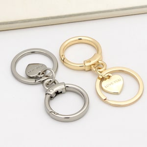 May include: Two keychains with heart-shaped charms. One keychain is silver with a charm that says "LOVE YOU". The other keychain is gold with a charm that says "LOVE YOU".
