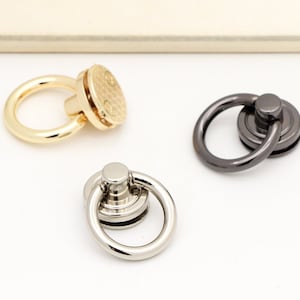 May include: Three metal ring clasps in gold, silver, and black finishes. Each clasp has a round ring and a decorative, textured base.