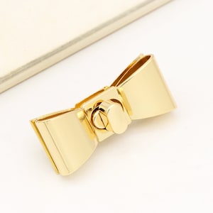 May include: Gold-toned metal bow-shaped clasp with a decorative twist lock.