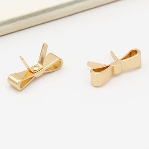 以下が含まれることがあります： 金色のリボン型のイヤリングのペア。イヤリングは金属製で、シンプルなデザインです。