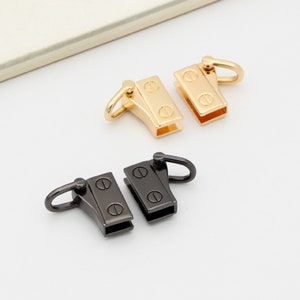 May include: Two sets of metal clasps, one gold and one black, with a swivel hook on each. The clasps are designed for attaching straps or handles to bags or other items.