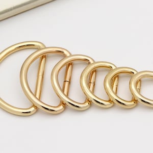 May include: Set of six gold-toned metal D-rings of varying sizes. The rings are arranged in a graduated size order, with the largest ring at the top and the smallest ring at the bottom.