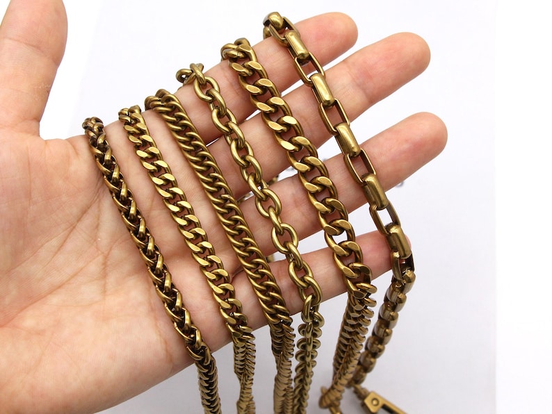K&ouml;nnte beinhalten: Eine Hand zeigt eine Auswahl an goldfarbenen Metallketten. Die Ketten variieren im Stil, einschlie&szlig;lich Panzer-, Seil- und Box-Link-Designs. Die Ketten sind wahrscheinlich f&uuml;r die Schmuckherstellung oder als dekorative Elemente gedacht.