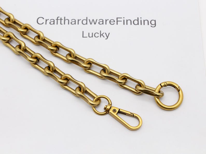 May include: A gold-colored chain with a lobster clasp and a circular clasp. The chain is made of interlocking rectangular links. The text "CrafthardwareFinding Lucky" is visible in the background.