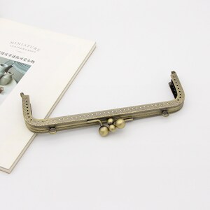 May include: A gold-toned metal purse frame with an ornate design and three decorative balls hanging from the center.