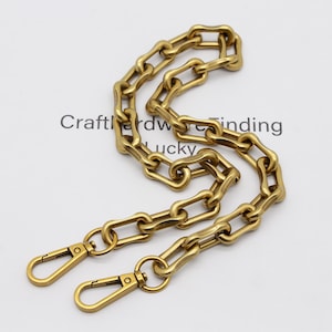 May include: A gold-colored chain with a series of elongated, rectangular links. The chain has two lobster claw clasps at the ends. The text "Crafthardware finding lucky" is visible in the background.