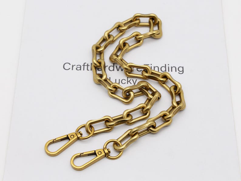 May include: A gold-colored chain with a series of elongated, rectangular links. The chain has two lobster claw clasps at the ends. The text "Crafthardware finding lucky" is visible in the background.