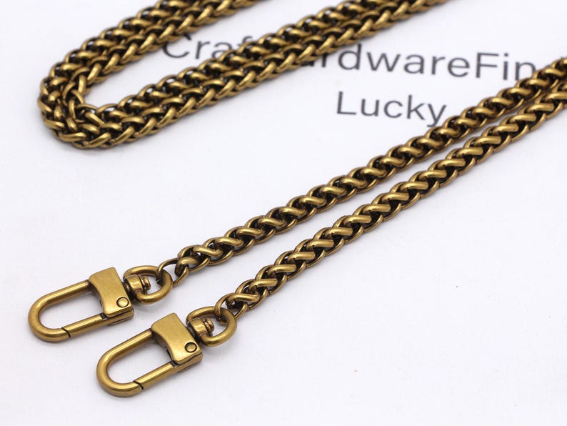 K&ouml;nnte beinhalten: Antik-messingfarbene Kette mit zwei passenden Verschl&uuml;ssen. Die Kette ist in einem gewebten Design gehalten, und die Verschl&uuml;sse sind im einfachen Hakenstil gehalten. Die Kette und die Verschl&uuml;sse befinden sich auf einer wei&szlig;en Oberfl&auml;che mit den W&ouml;rtern "Craft Hardware Fin" und "Lucky".