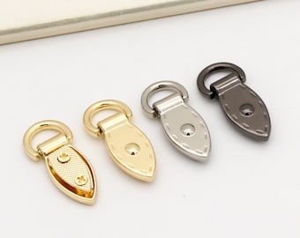 May include: Four metal purse or bag hardware pieces in different finishes: gold, silver, nickel, and black. Each piece has a D-ring and a decorative oval shape with stitching detail.
