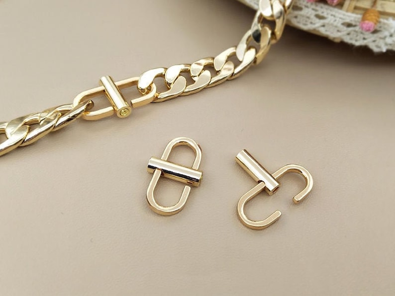 May include: Two gold-toned metal clasps, one with a single loop and the other with a double loop. The clasps are commonly used for attaching straps or chains to bags or other accessories.