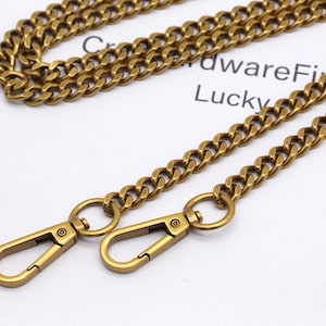 K&ouml;nnte beinhalten: Nahaufnahme einer goldfarbenen Kette mit zwei Karabinerverschl&uuml;ssen. Die Kette besteht aus ineinandergreifenden Gliedern und hat ein Vintage-Aussehen. Im Hintergrund ist der Text "HardwareFi Lucky" zu sehen.