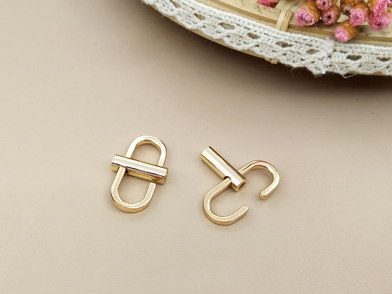 May include: Two gold-toned metal clasps, one with a straight bar and the other with a curved hook.