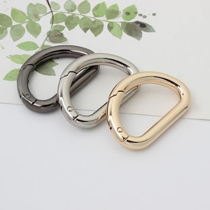 Peut inclure: Trois fermoirs en D métalliques dans différentes finitions : gris foncé, argent et or. Les fermoirs sont ouverts et prêts à être fixés à un sac, un porte-monnaie ou un autre article.