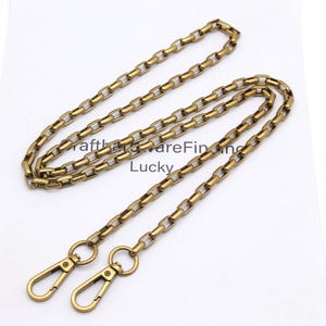 K&ouml;nnte beinhalten: Eine goldfarbene Metallkette mit rechteckigen Gliedern und zwei passenden Verschl&uuml;ssen. Die Kette liegt auf einer wei&szlig;en Oberfl&auml;che. Der Text "CrafthardwareFinding Lucky" ist sichtbar.