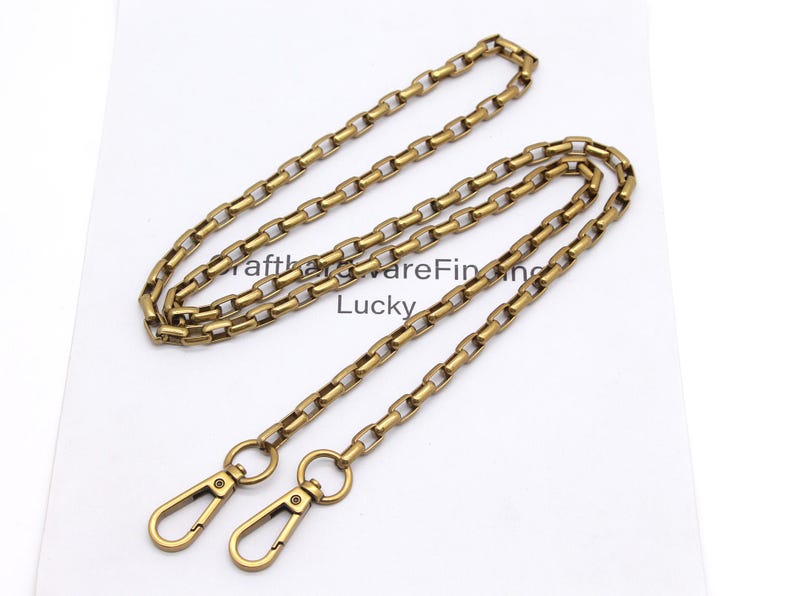 K&ouml;nnte beinhalten: Eine goldfarbene Metallkette mit rechteckigen Gliedern und zwei passenden Verschl&uuml;ssen. Die Kette liegt auf einer wei&szlig;en Oberfl&auml;che. Der Text "CrafthardwareFinding Lucky" ist sichtbar.