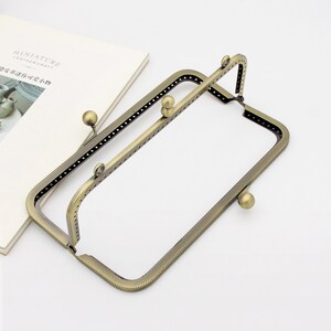 May include: A pair of antique gold-toned metal purse frames with a textured finish. The frames are open and ready to be assembled.