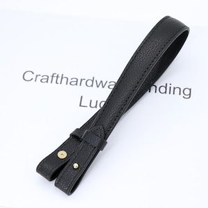 Könnte beinhalten: Schwarzer Leder-Taschengriff mit goldfarbenen Nieten. Der Griff besteht aus strukturiertem Leder und hat ein Schlaufendesign. Der Text "Crafthardwa...ding" ist im Hintergrund sichtbar.