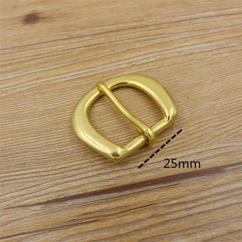 Puede incluir: Una hebilla de metal dorado de forma rectangular redondeada. La hebilla mide 25 mm de ancho.