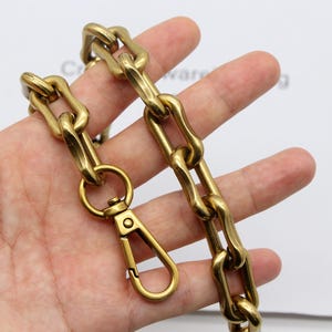 May include: A heavy-duty, gold-colored chain with a matching clasp. The chain links are thick and oval-shaped. The clasp is a spring-loaded design for secure attachment. The chain is likely used for bags, wallets, or other accessories.