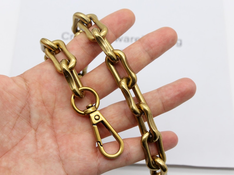 May include: A heavy-duty, gold-colored chain with a matching clasp. The chain links are thick and oval-shaped. The clasp is a spring-loaded design for secure attachment. The chain is likely used for bags, wallets, or other accessories.