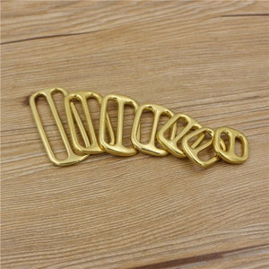 May include: A set of eight gold-toned metal D-rings of varying sizes. The rings are arranged in a row from largest to smallest.